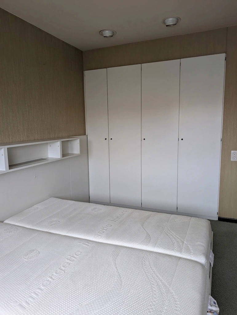Ingebouwde witte kasten en bed, gezien vanop afstand